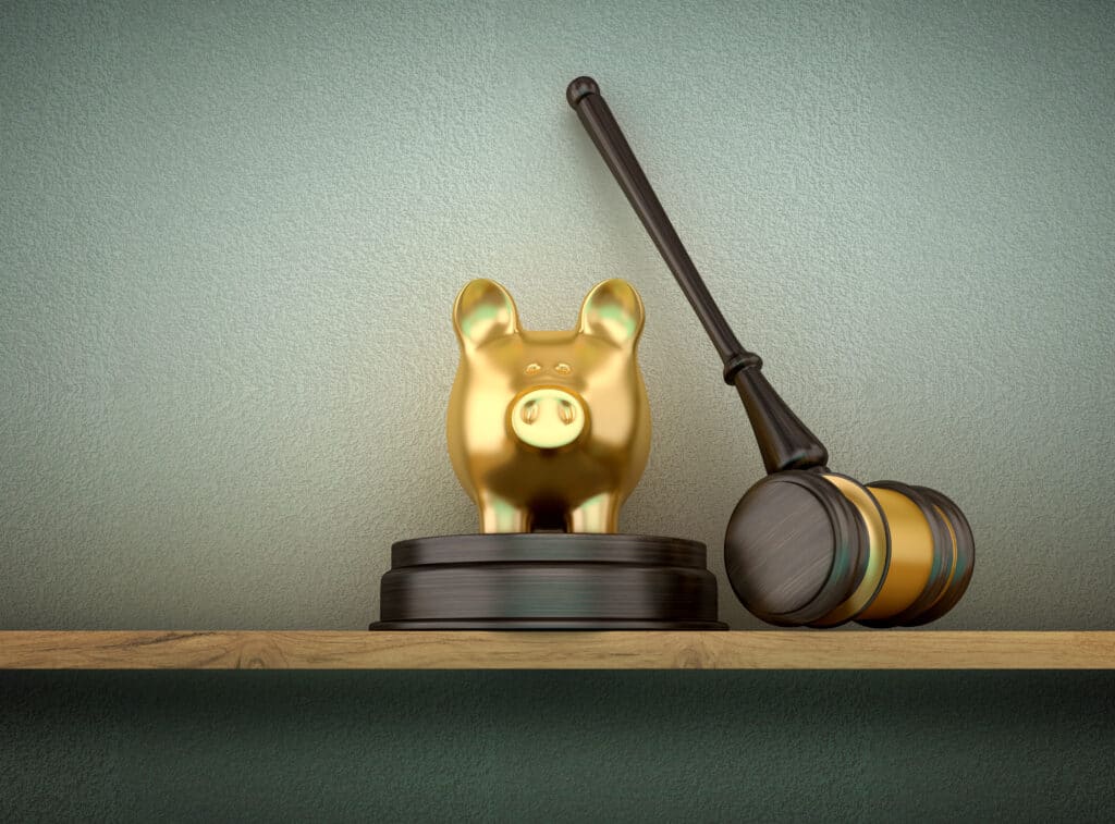 Ein goldenes Sparschwein steht neben dem Hammer eines Richters, symbolisiert Geld und Gerechtigkeit.